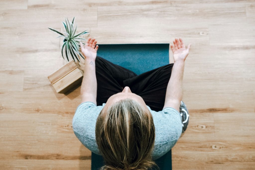 a person sitting on a yoga mat in meditation pose with plant beside them