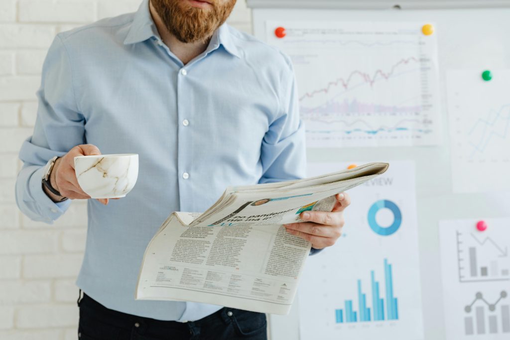 A person with a job in business administration reads a newspaper with business charts and coffee.