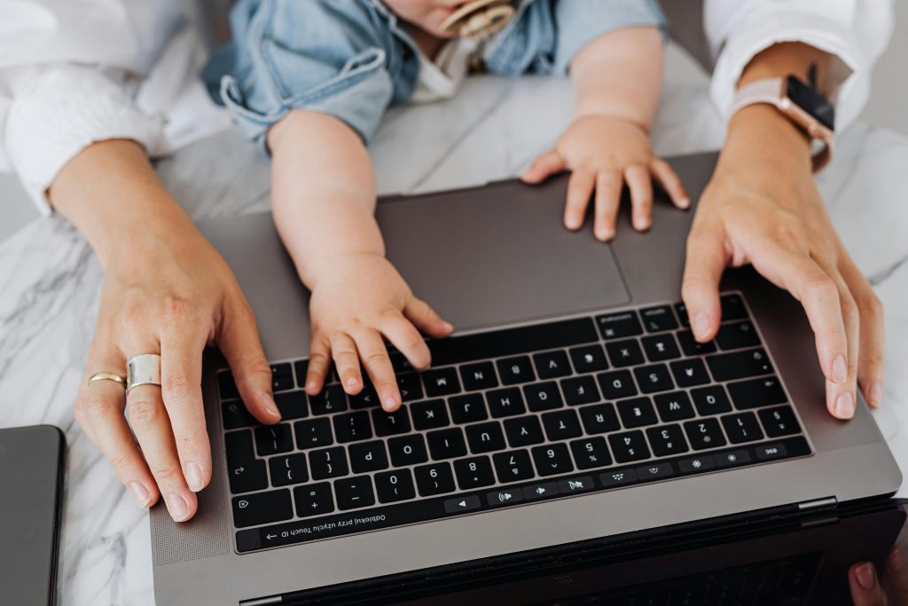 A single mom taking online courses looking at a computer screen while studying with her children on the couch.