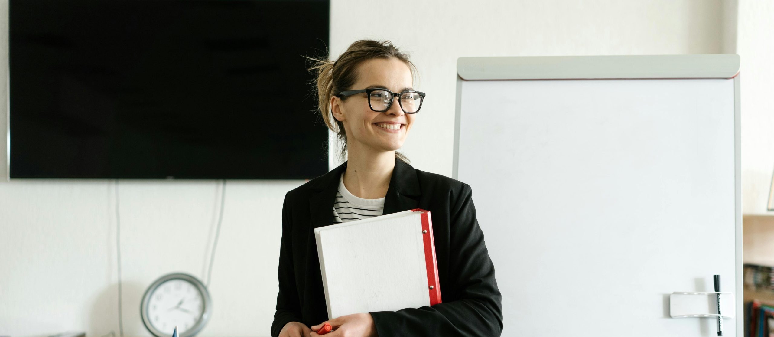 a woman teacher in black with glasses, standing at the front of her classroom with a successful teacher resume