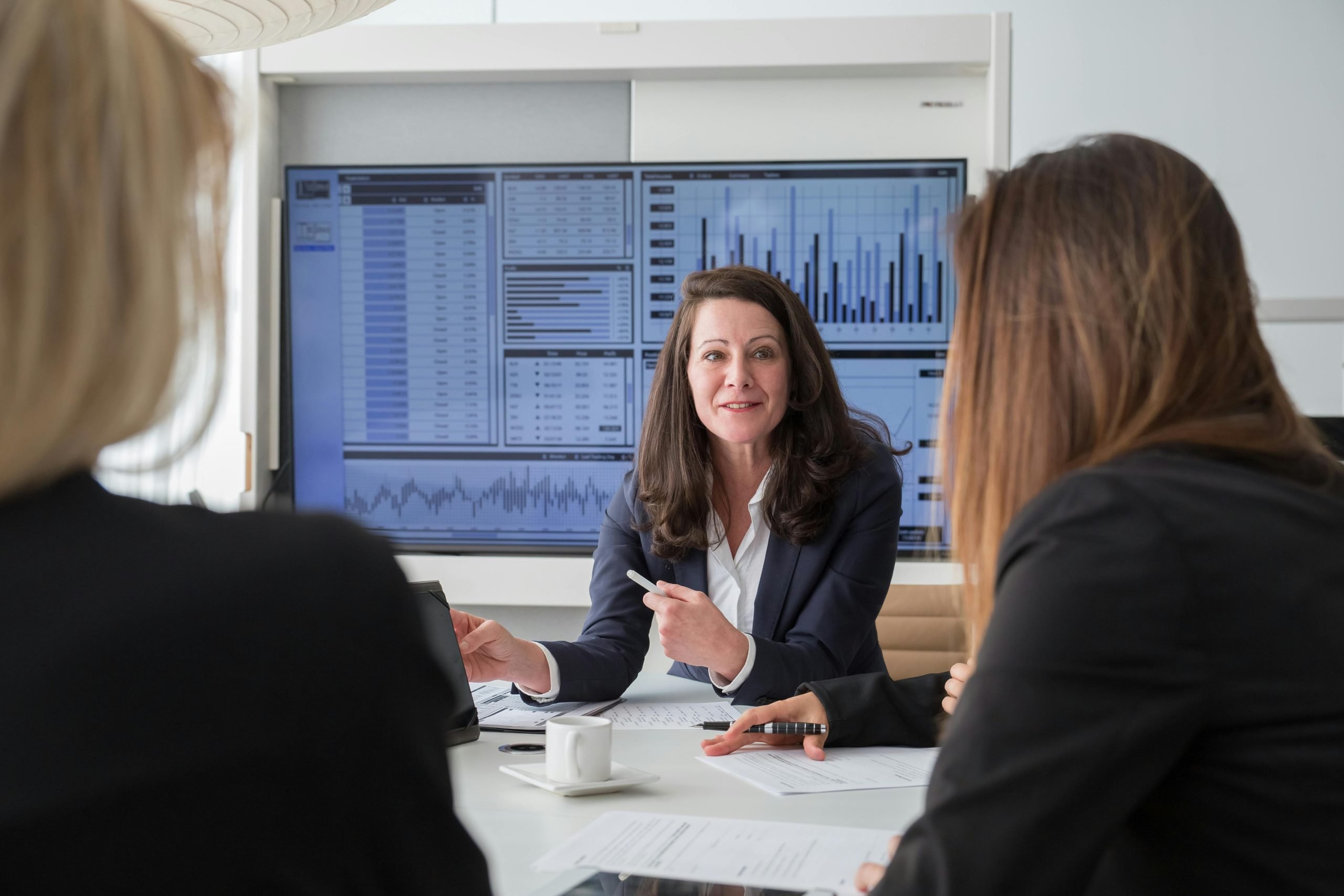 three women in conference room meeting with charts displayed in the background