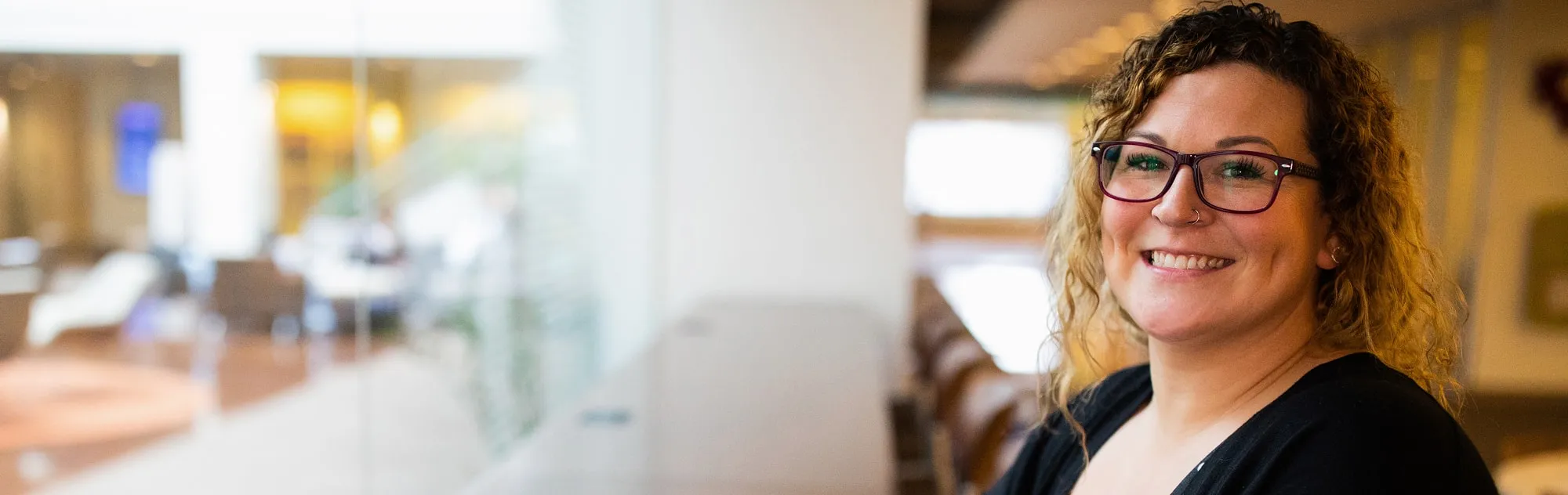 Woman with glasses in study hall looking into camera.