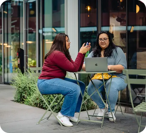 Two students sitting at a cafe table outside with their devices for studying.